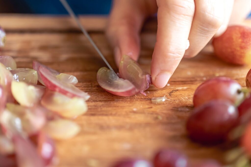 Person cutting a grape into a small piece before offering it to a rabbit illustrating the correct portion size for safe introduction